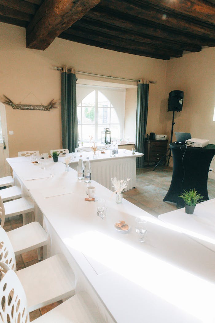 Bright conference room setup with elegant decor featuring white tables and rustic wooden beams.